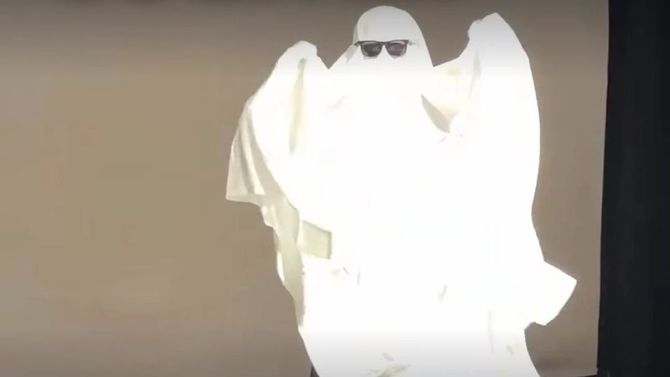 A golfer in a bedsheet ghost costume and sunglasses in a simulator bay